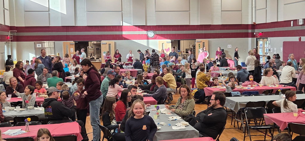 A crowd of families in a school cafeteria for a community dinner.