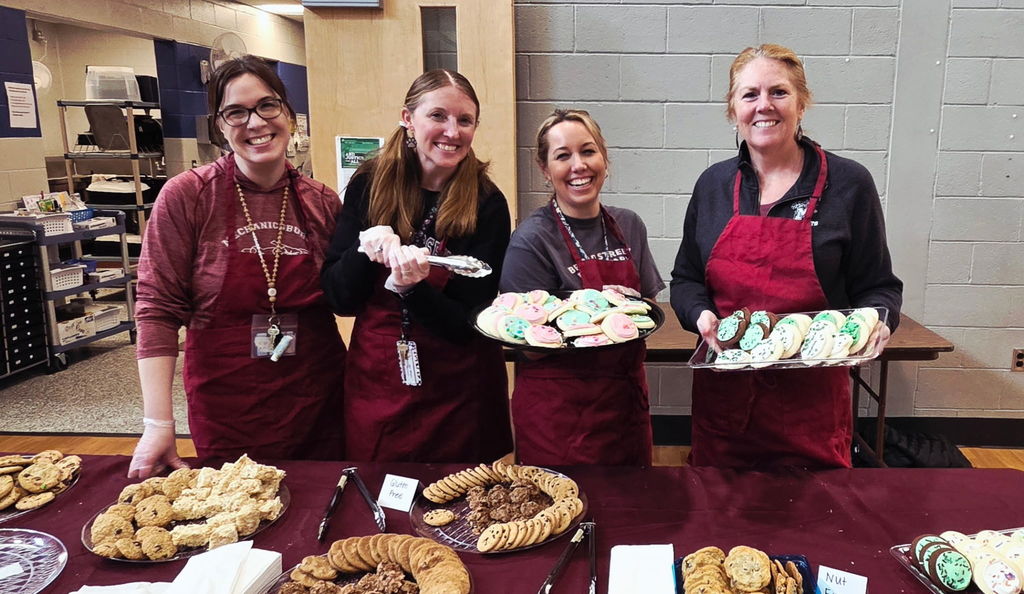 Staff holding trays of cookies in a school cafeteria.