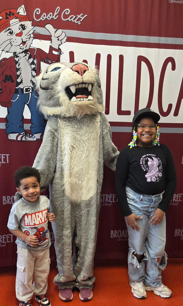 Two young children standing next to a wildcat mascot.