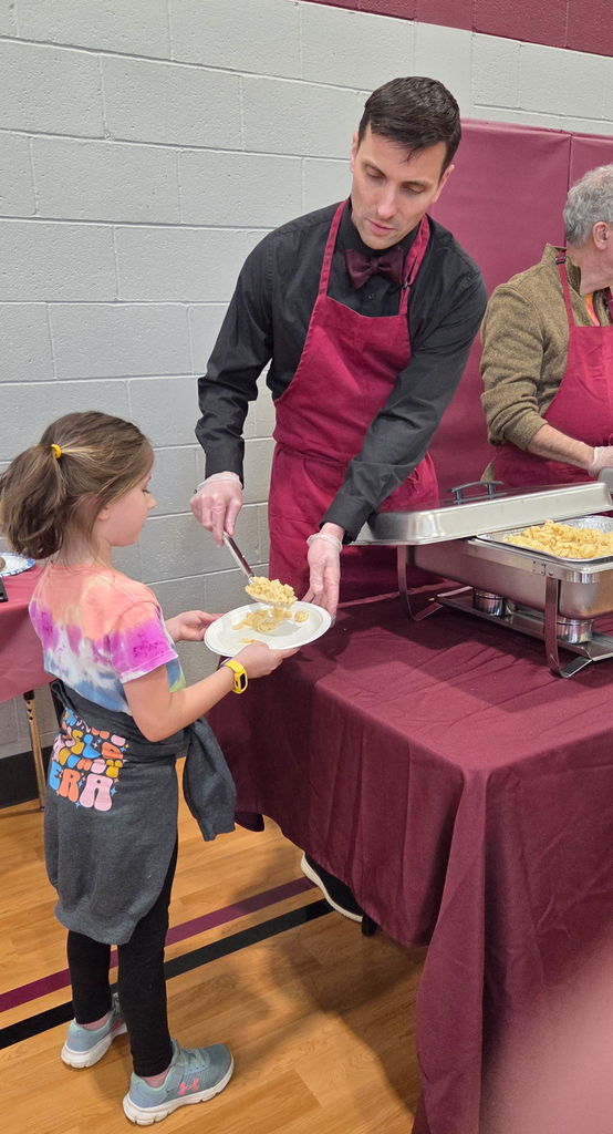 A man serving a young student macaroni and cheese.