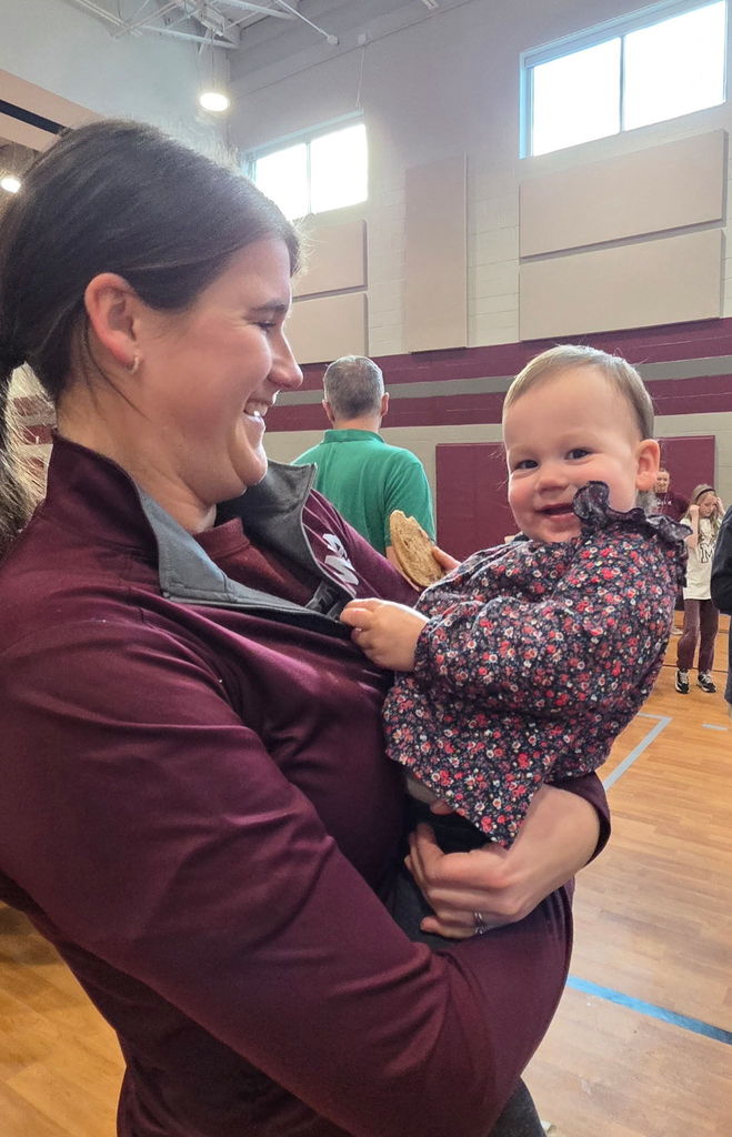 A little girl holding a cookie and being held by a smiling adult.