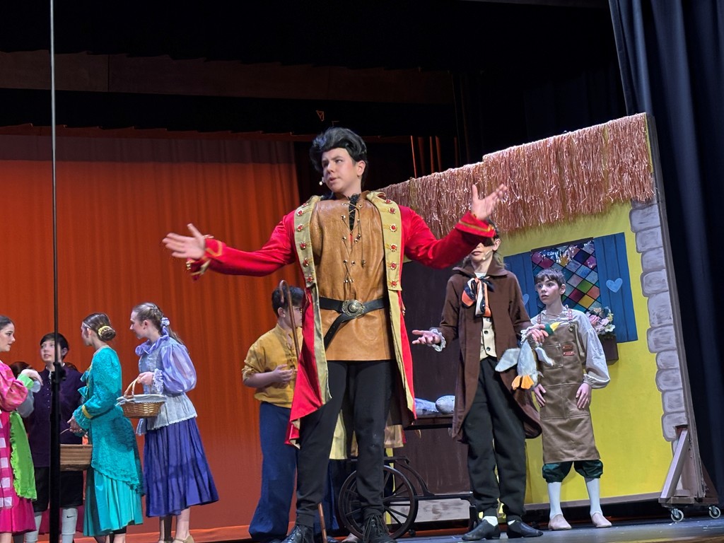 Students on stage in colorful Beauty and the Beast costumes.