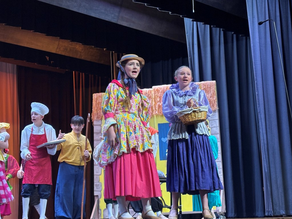 Students on stage in colorful Beauty and the Beast costumes.