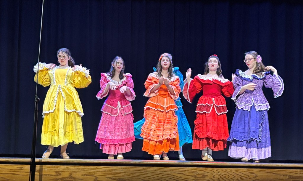 Students on stage in colorful Beauty and the Beast costumes.