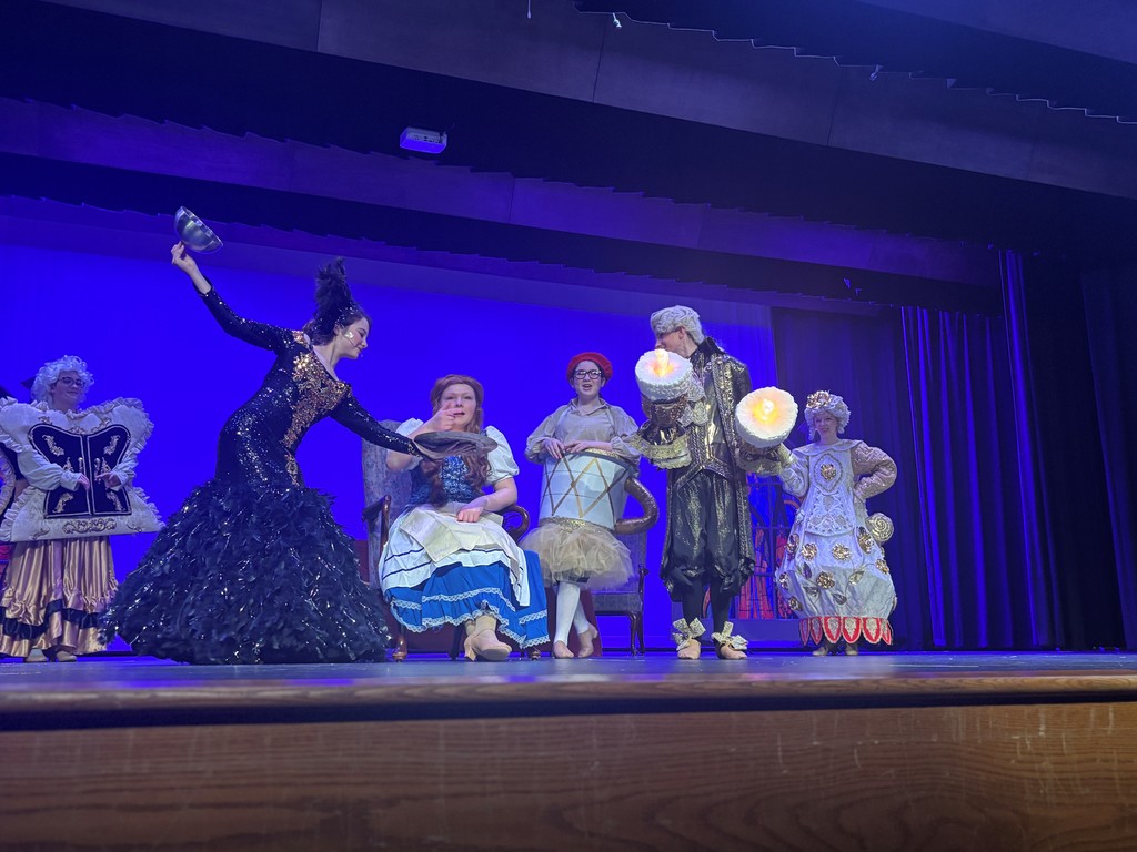 Students on stage in colorful Beauty and the Beast costumes.