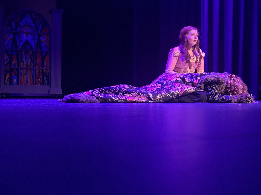 Students on stage in colorful Beauty and the Beast costumes.