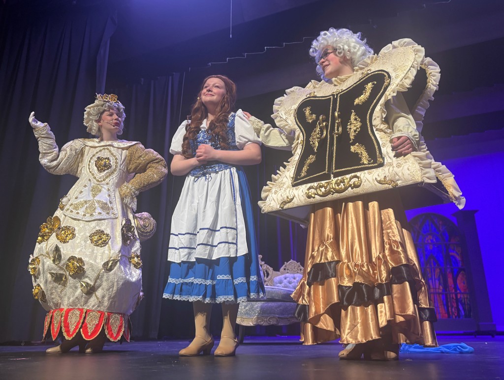 Students on stage in colorful Beauty and the Beast costumes.