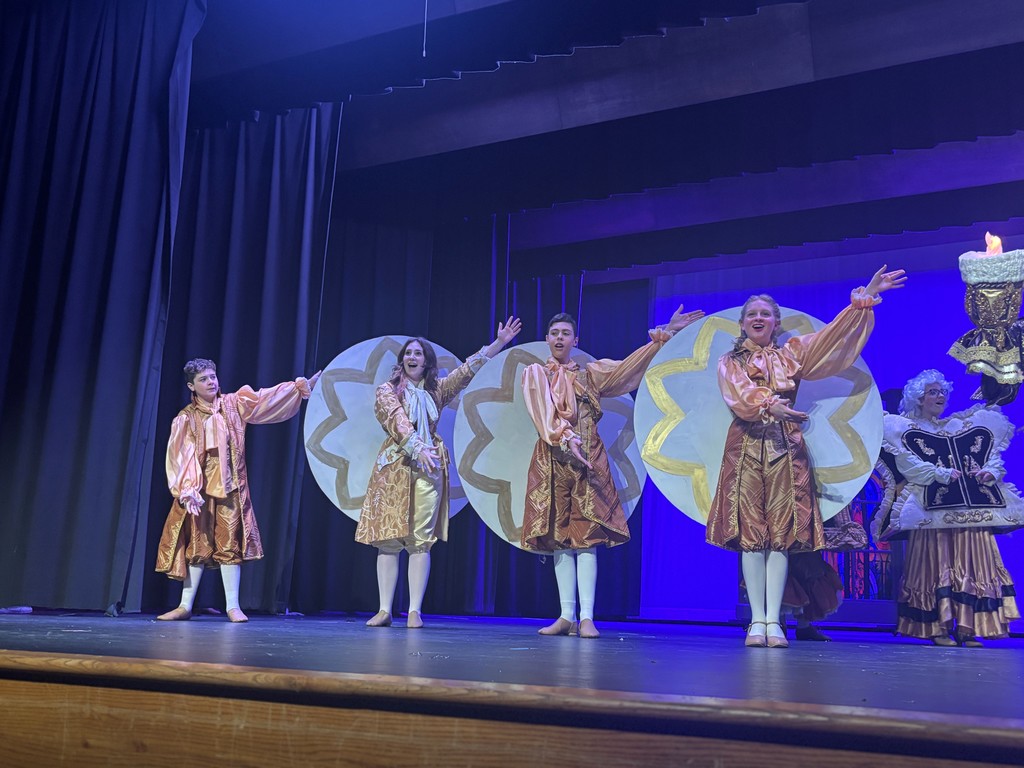 Students on stage in colorful Beauty and the Beast costumes.