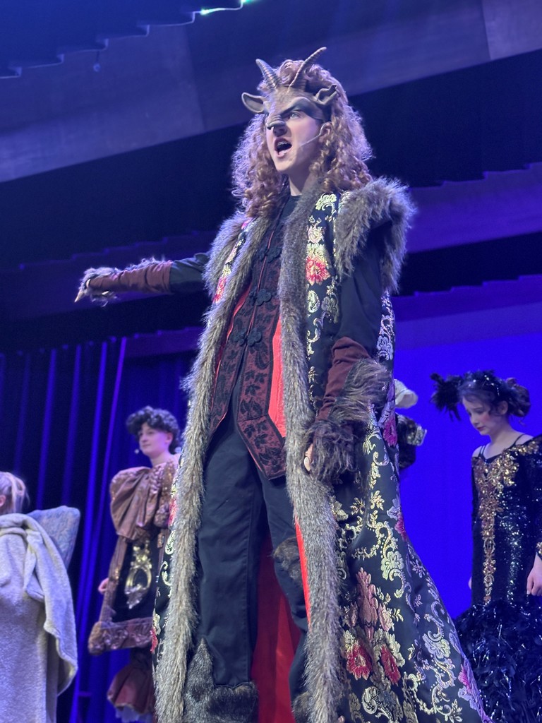 Students on stage in colorful Beauty and the Beast costumes.