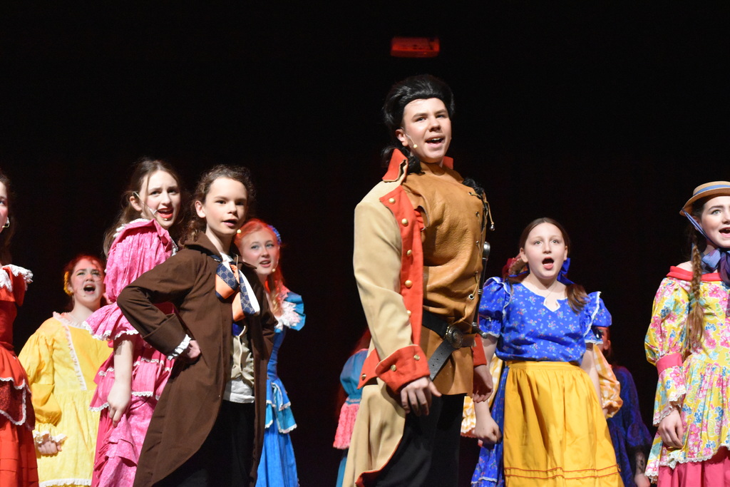 Students on stage in colorful Beauty and the Beast costumes.