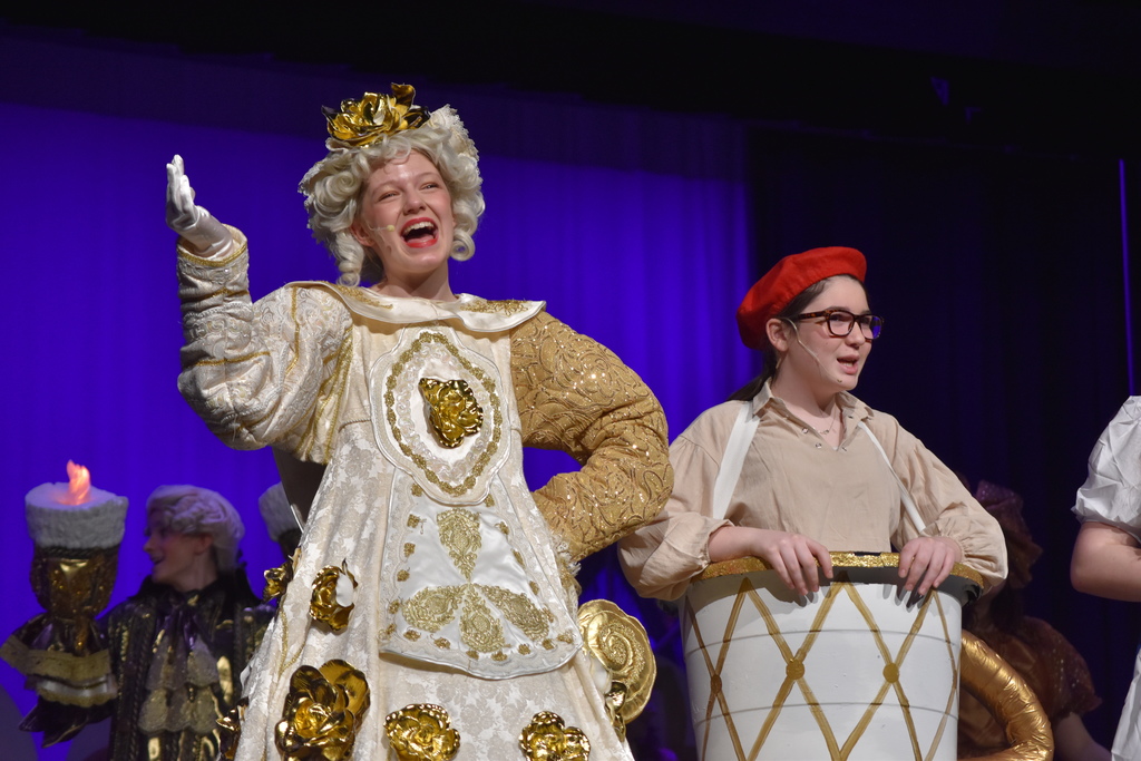 Students on stage in colorful Beauty and the Beast costumes.