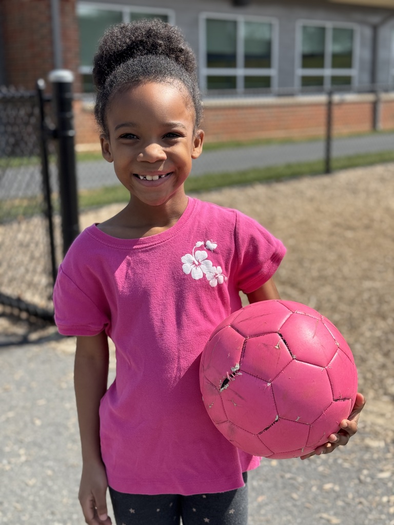 A happy and smiling young girl in a bright pink shirt holding a bright pink soccer ball.