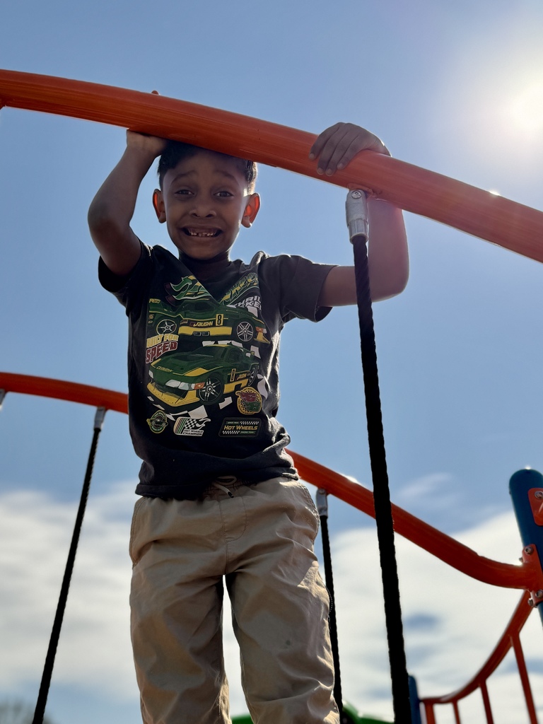 A young boy on a jungle gym on a school playground.