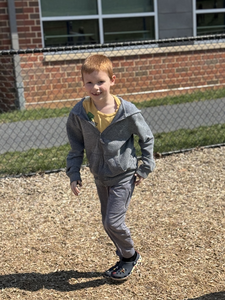 A happy and smiling young boy running around a school playground.