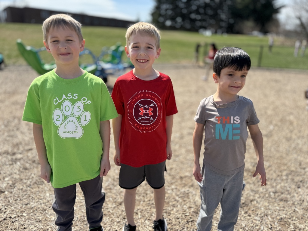 Three young boys in colorful shirts on a school playground.