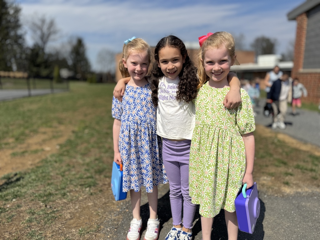 Three young girls standing arm in arm on a school playground.