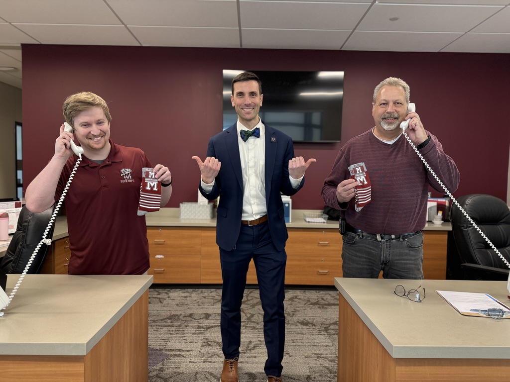 Two men holding phones and socks, while another man in a suit smiles and points to them.