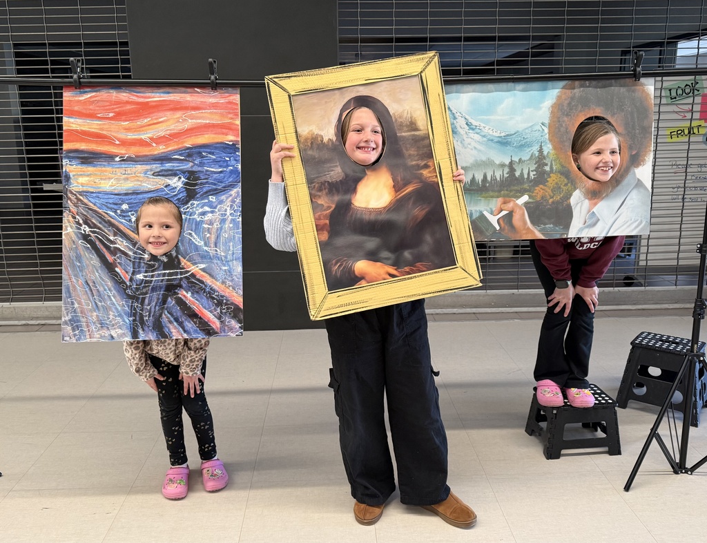 Students with their heads in cardboard cutouts of paintings.
