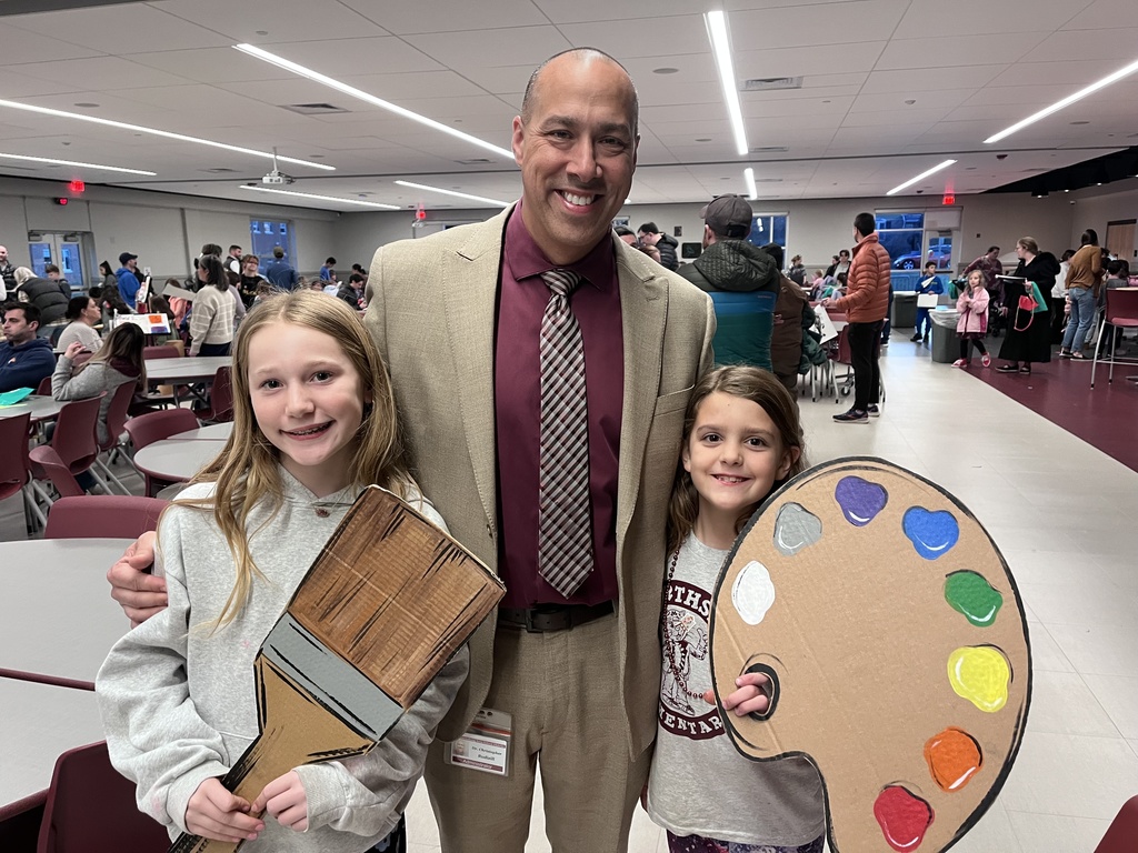Two students holding cardboard art supplies while standing next to a man in a suit.