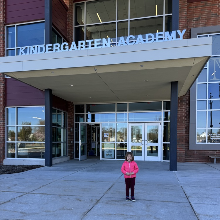 a little girl stands in front of an elementary school.