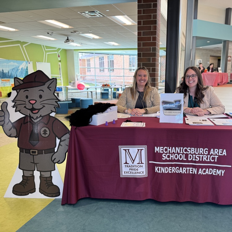 two female staff members sit at a table to greet incoming students.