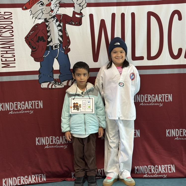 Young students standing in front of a wildcat banner.