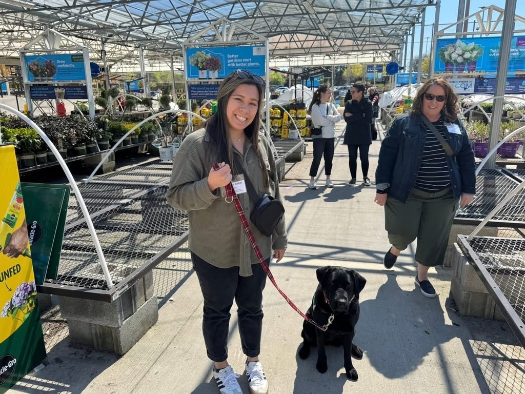 Adults walking through a gardening section of a store with their facility dog.