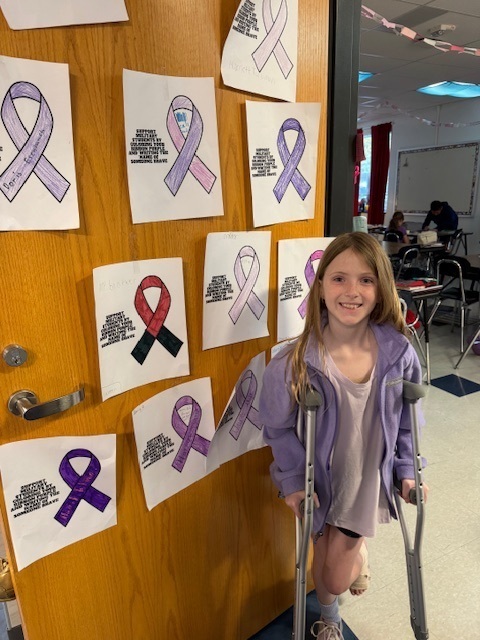A young student wears purple while standing next to a wall of purple ribbons.