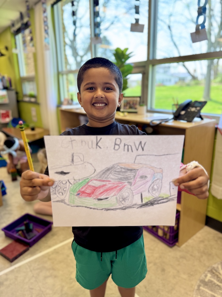 A young student proudly holds up a picture he drew of a colorful car and truck.