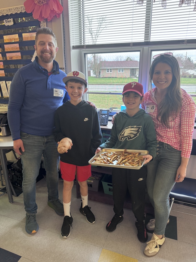 Two students with. two adult volunteers holding a potato and tray of homemade french fries.