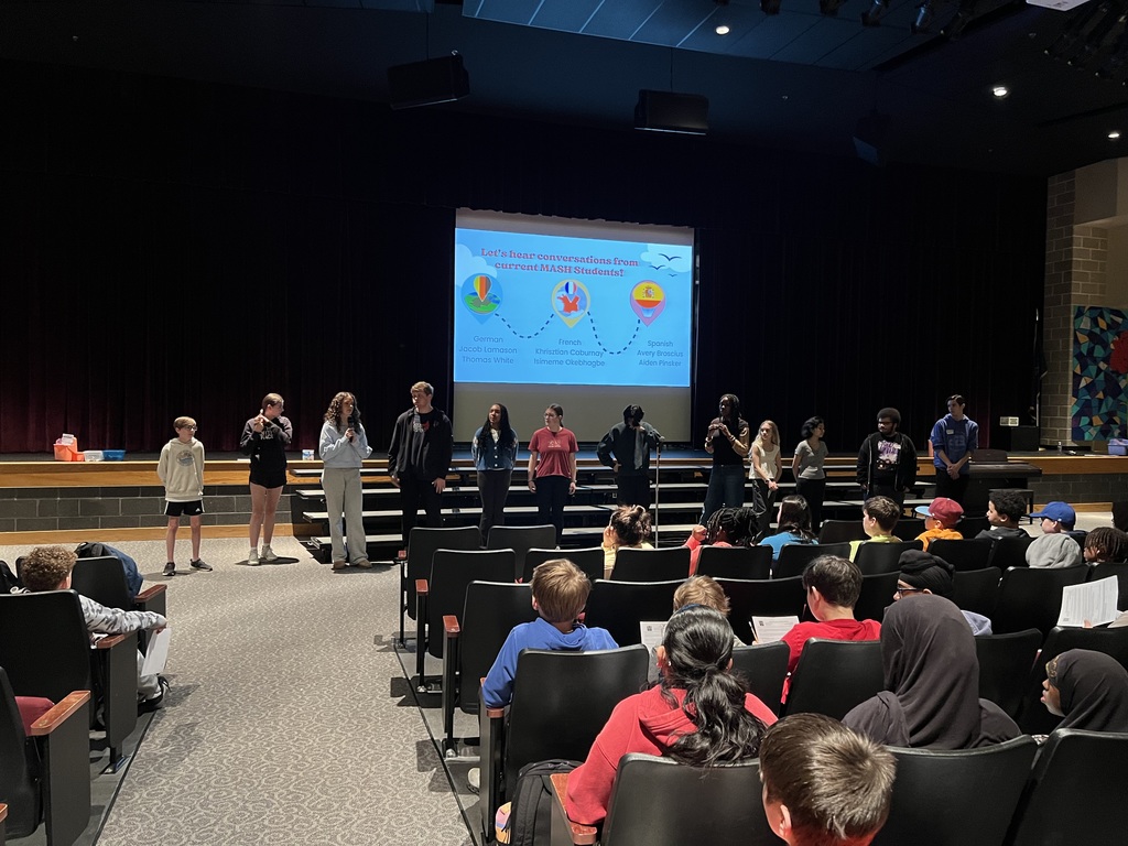 Students stand in front of a screen and audience to give a presentation.