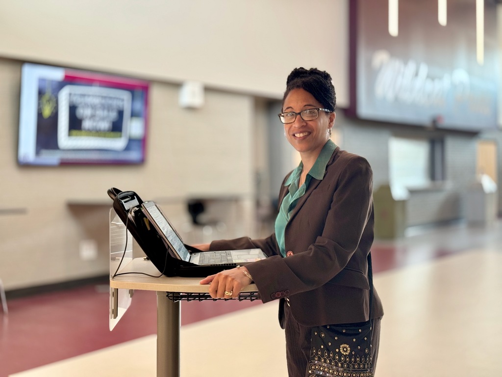 An assistant principal with a laptop cart rolling down a hallway.