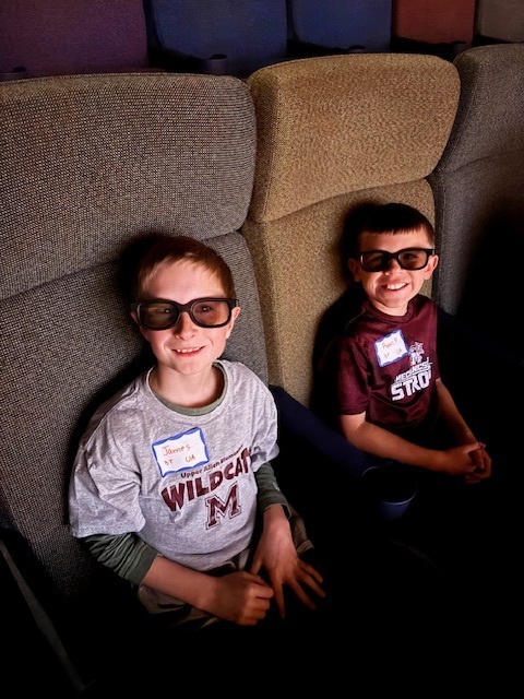 Students seated in an iMAX theater and wearing their 3D glasses.