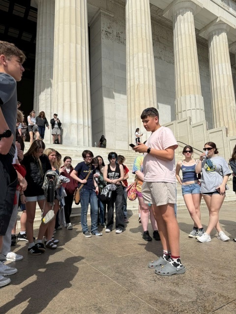 A student reading a speech to a crowd while standing in front of the Lincoln Memorial.