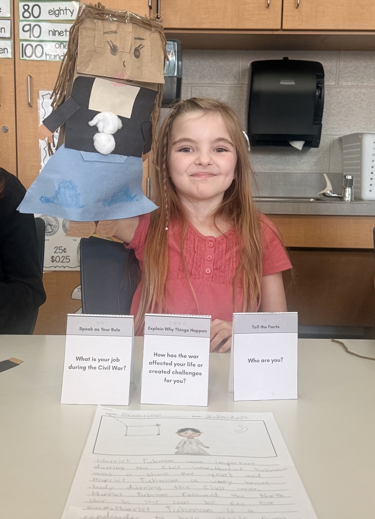 A young students holds up a paper puppet of Harriett Tubman.