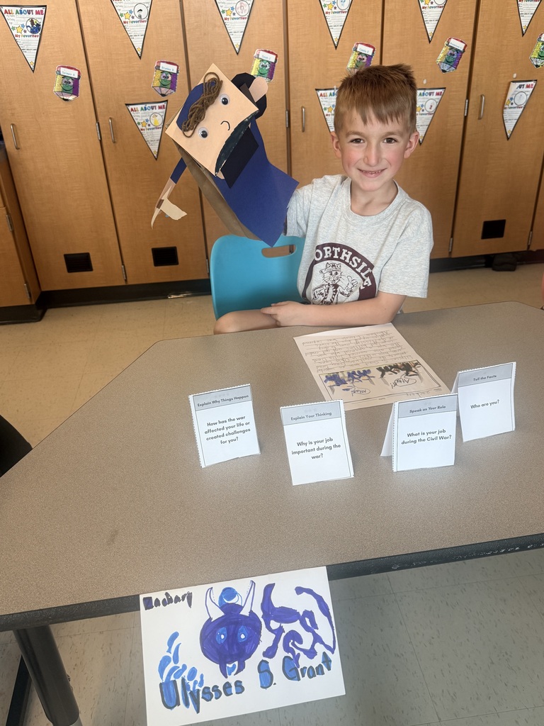 A young students holds up a handmade paper puppet of Ulysses S. Grant.