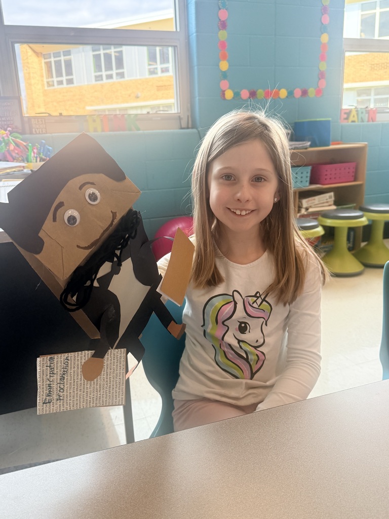 A young girl holds up a handmade paper puppet.