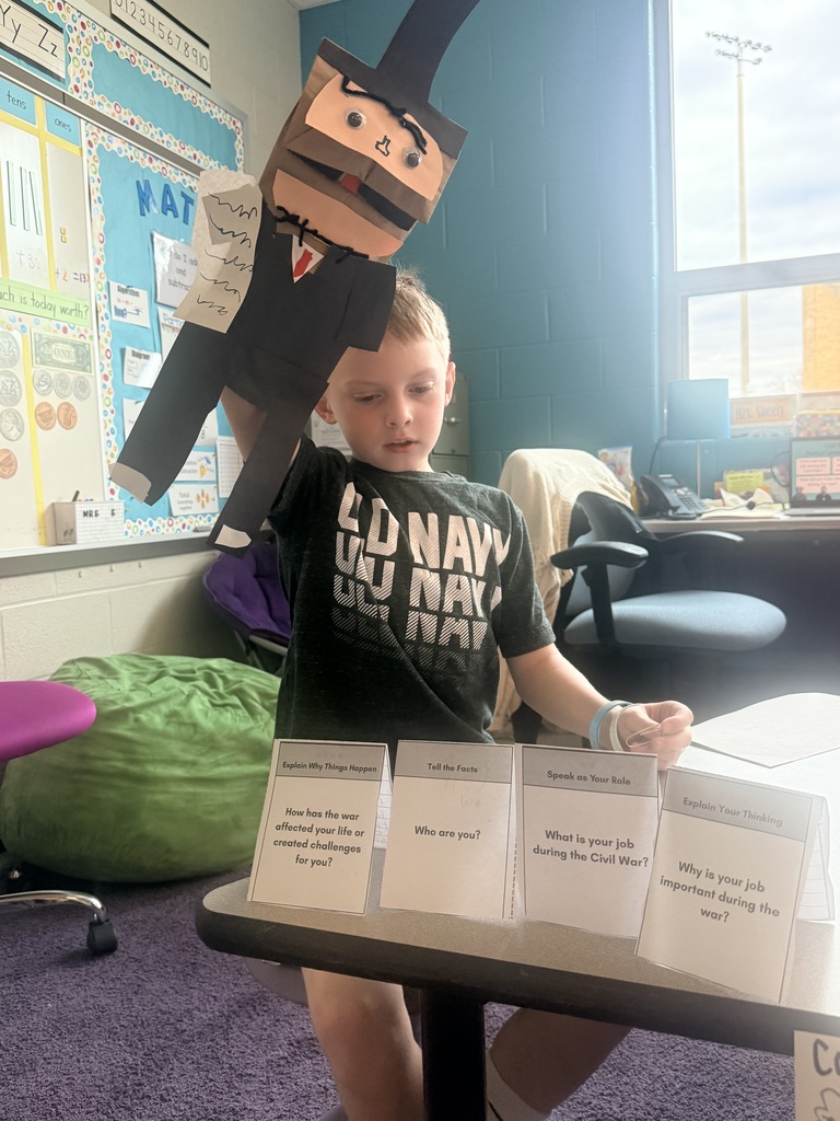 A young boy holds up a handmade paper puppet.
