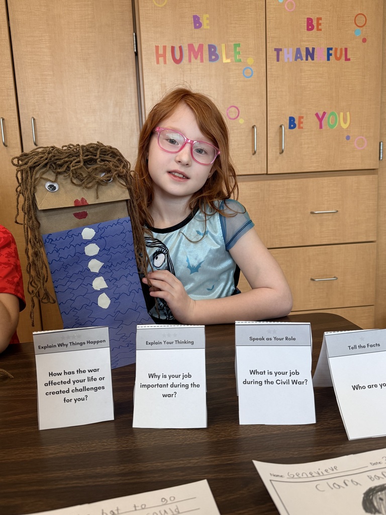 A young girl holds up a handmade paper puppet.