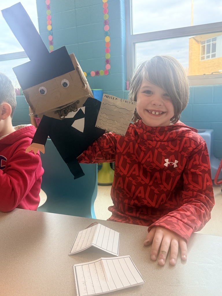 A young boy holds up a handmade paper puppet.