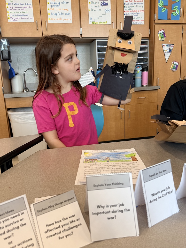 A young girl holds up a handmade paper puppet.