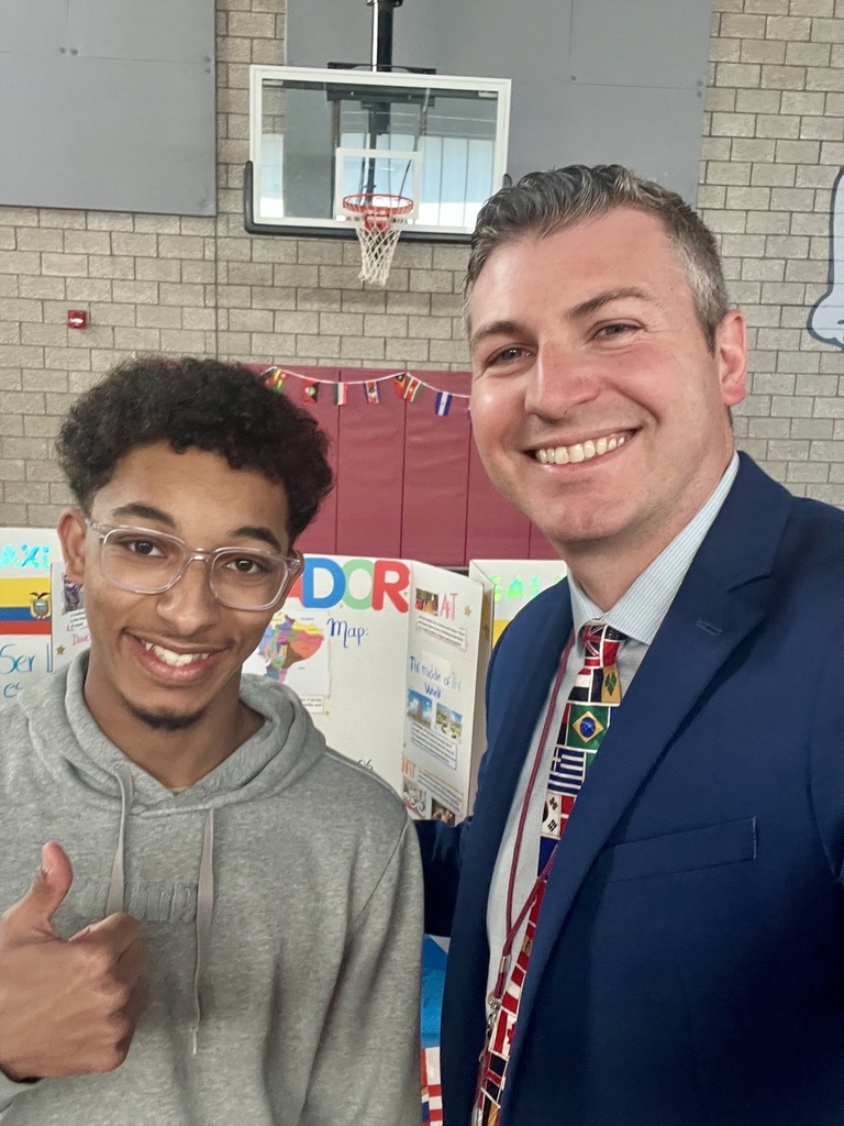 A man in a suit and  a student with a thumbs up both smiling for a selfie.