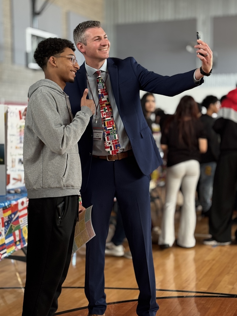 A man in a suit lining up the perfect selfie with a student who is giving a thumbs up.