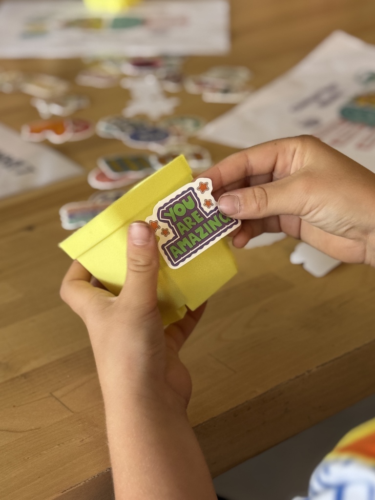 A students puts a "You Are Amazing" sticker on a yellow flower pot.
