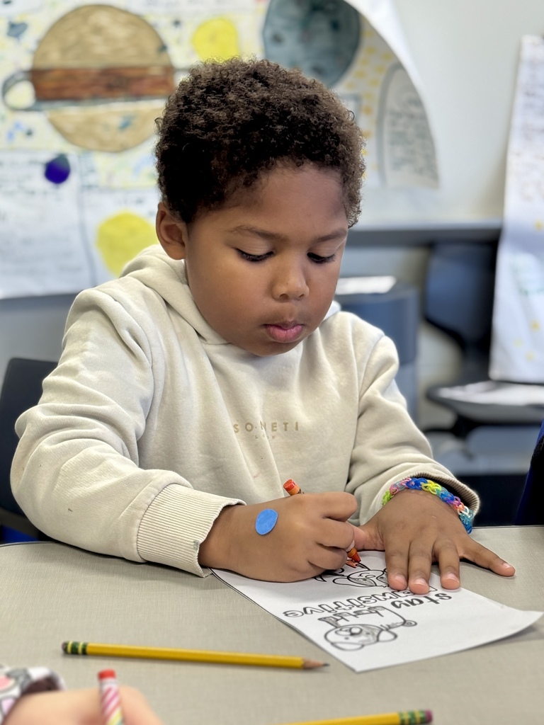 A young student sits at a table and colors a worksheet.