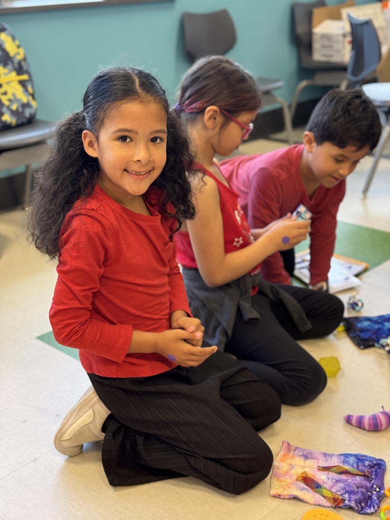 A young student on the floor with friends smiles for the camera.