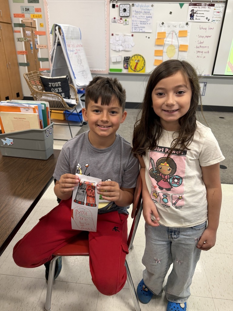 Two students side by side as one holds a handwritten card the other made.
