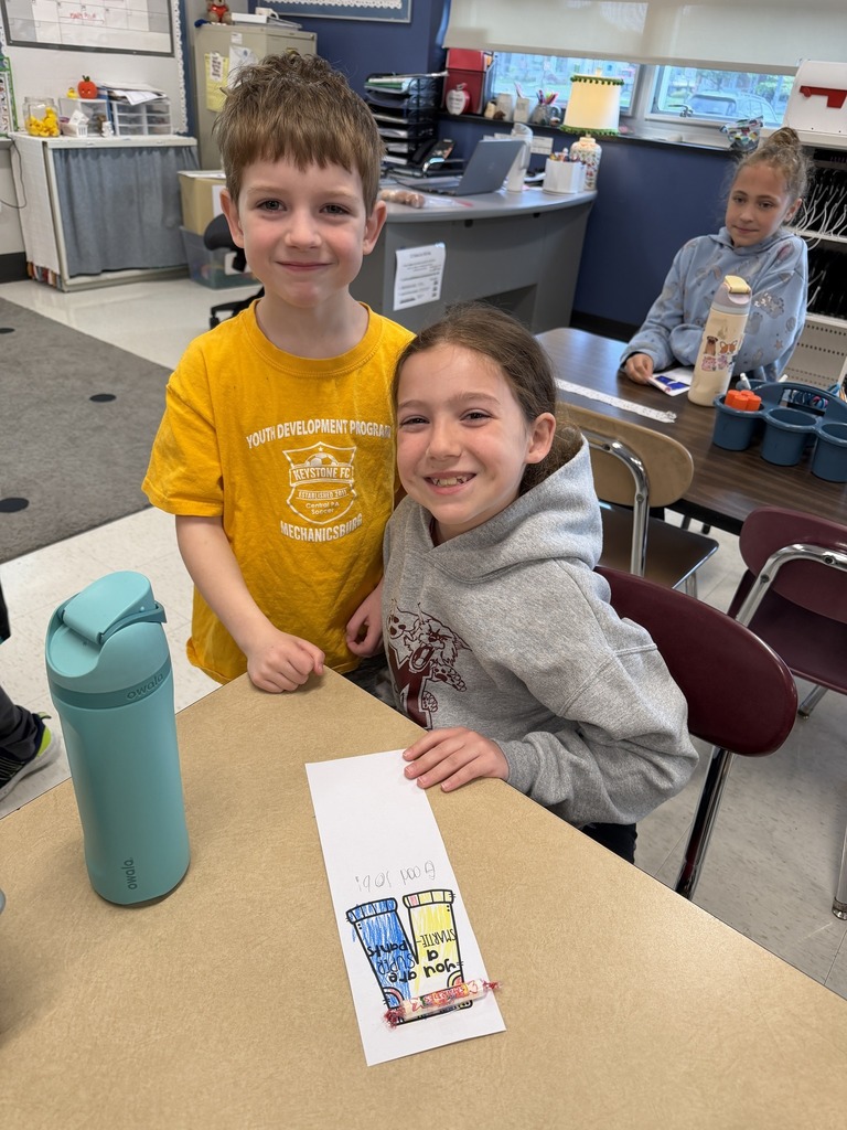 Two students side by side as one holds a handwritten card the other made.
