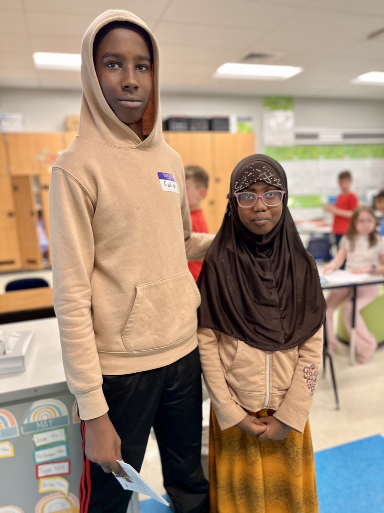 A younger and older student pose for a photo after the older student read a book he wrote to the younger student.