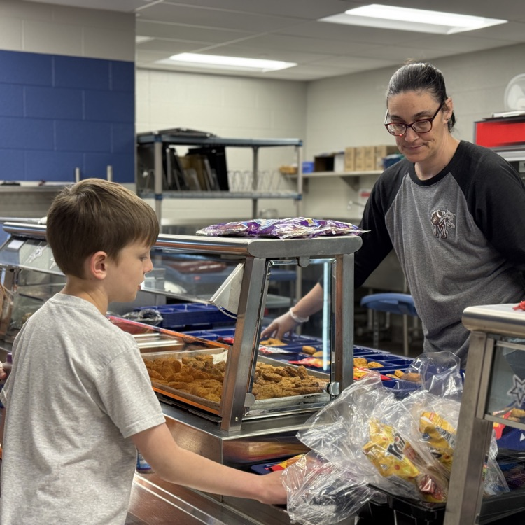 A lady serves lunch in a school cafeteria